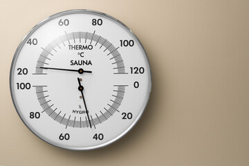 Close-up of an analog sauna thermo-hygrometer with a metal ring on a beige background. Copy space. High resolution.