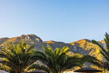 Beautiful view of sunlit mountains with palm trees and clear blue sky in warm tropical landscape. Kos. Greece.