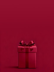 Obraz premium Elegant deep red gift box with satin ribbon and bow against a matching solid background