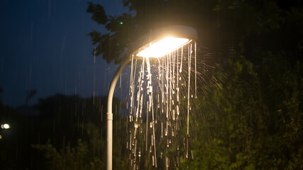 Modern street lamp glowing bright during heavy rain shower at night with falling water drops