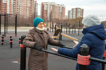 An elderly woman exercising on parallel bars with her daughter on a street sports ground. Active lifestyle and sport for senior generation outside.