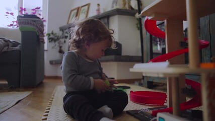Toddler sitting on floor examining small toy with focused curiosity showing independent play and quiet concentration during everyday home moment