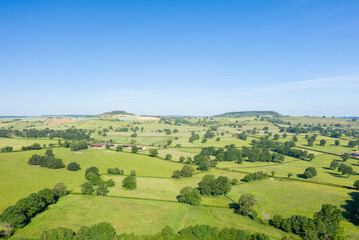 Fototapeta premium Wide aerial view of lush green fields divided by hedgerows and dotted with trees under a clear blue sky in the Nivernais countryside.