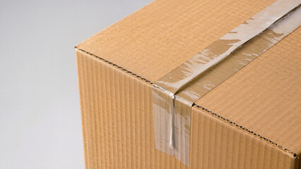 A detailed view of the corner of a brown corrugated box with clear packaging tape. Minimalistic light background. Ideal for logistics, moving, product delivery, and e-commerce.