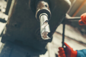Low angle view of metal industrial drill bit protruding from manufacturing machine inside factory.