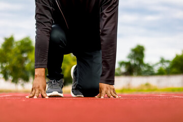 Athlete on starting line crouched, ready to sprint on red track, outdoor sports