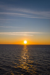 Obraz premium Golden sunlight stretches across calm open water as the sun sets above the horizon, creating a luminous path between the Adriatic and Ionian Seas. Wispy clouds and a gradient sky enhance the serene