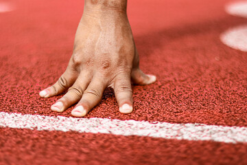 Athlete's Hand on Starting Line of Red Running Track Ready to Sprint