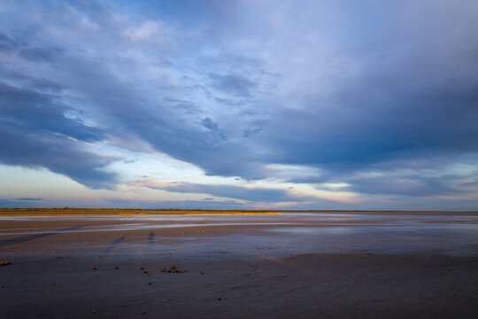 Expansive wet sands in Camargue reflect the soft hues of an evening sky filled with sweeping blue and lavender clouds, creating a peaceful and open coastal mood.