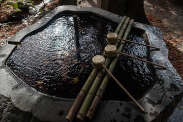 Japanese stone water basin. Bamboo ladles rest neatly on bamboo supports above water Gentle ripples on surface suggest recent use, symbolizing purification, mindfulness, and quiet reflection  