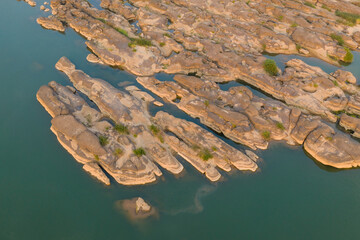 Aerial view of elongated sandstone ridges and shallow pools along the Mekong River near Champassak in southern Laos. Warm evening light reveals natural rock textures, subtle greenery, and tranquil