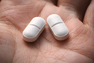 Two White Oval Shaped Pills with a Score Line Held Gently in the Palm of a Human Hand, Macro Shot