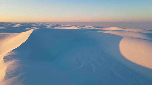 Wide aerial panning shot tracking slowly over vast untouched white desert sand dunes or pristine snow fields creating a serene minimal horizon terrain, sweeping view, wilderness