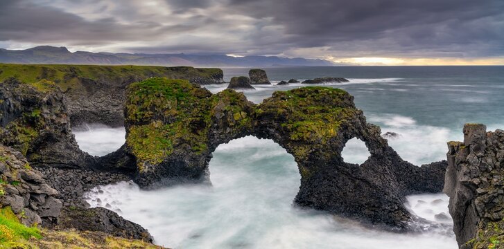 panorama view of the wild and rugged coastline near Arnarstapi with the landmark Gatklettur sea arch on a stormy overcast summer morning