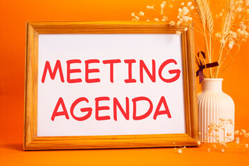 Meeting agenda symbol. Concept words Meeting agenda on beautiful wooden picture frame. Beautiful orange background with flower vase. Business and Meeting agenda concept. Copy space.