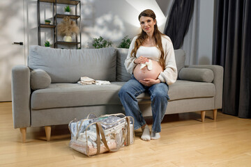 Expecting mother sits on sofa with packed hospital bag nearby, preparing for childbirth and new beginnings