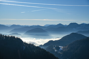 Picturesque Alpine landscape in the Bavarian mountains with valleys covered by a thick blanket of fog, while the peaks are bathed in bright sunlight. Blue sky with contrails.