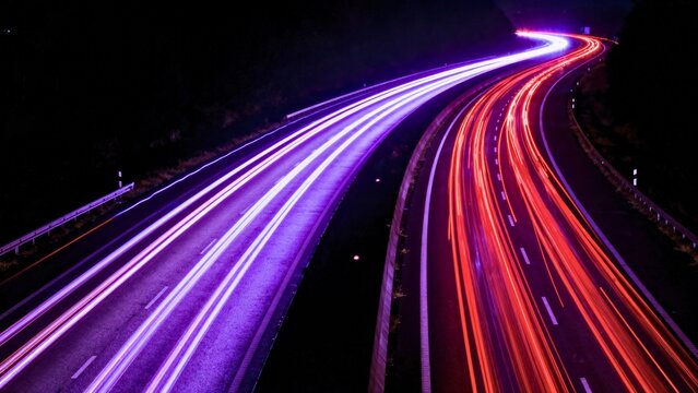A long exposure of a highway at night with extreme saturation. Brake lights streak ruby red, headlights glow violet-white, floating in deep black void.
