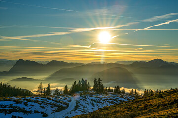Picturesque sunset over a mountain landscape in the Chiemgau Alps with snow-covered slopes and fog in the valleys in the golden evening light with orange coloring of the sky (evening glow)