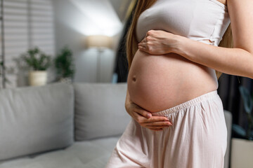 Close-up of pregnant woman's belly with hands gently cradling it, indoors with soft lighting and blurred background elements