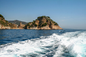 Fototapeta premium Sunny day on the Mediterranean coast with rocky cliff, historic tower, and blue sea. Idyllic travel scenery in Spain, vibrant beach, clear sky, and summer vacation destination.
