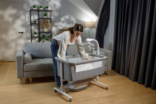 Pregnant woman arranging baby crib with mobile in nursery room preparing for newborn arrival