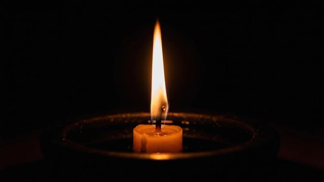 A single lit candle in a dark room with a warm glow emanating from the flame