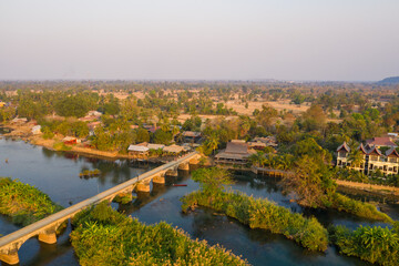 Fototapeta premium Aerial perspective reveals the historic French colonial bridge connecting Don Det and Don Khon in the 4000 Islands, southern Laos. Warm daylight highlights riverside houses, lush greenery, and