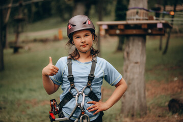 Confident Girl Giving OK Sign in Safety Harness at Adventure Park