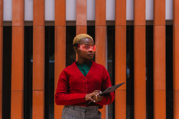 Black woman wearing red cardigana and augmented reality glasses, holding a tablet