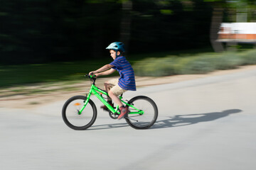 Fototapeta premium Young boy riding bicycle in park wearing helmet at speed