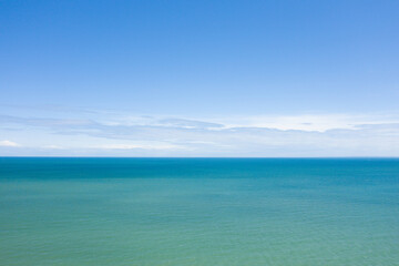 Fototapeta premium Minimalist seascape with tranquil turquoise water stretching to the horizon beneath a bright, cloud-dappled sky in daylight. The scene evokes a sense of peace and open space.