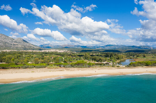 Vibrant turquoise sea meets a wide sandy beach with Orosei town and rugged mountains in the background. Lush greenery and dramatic clouds add depth to this bright Mediterranean coastal scene. - Powered by Adobe