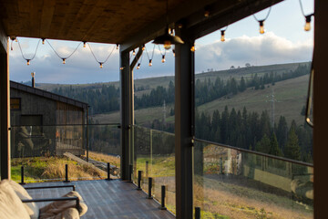 Terrace offering view of rolling green hills and dense forest in mountains, strings of lights hanging above, creating cozy atmosphere