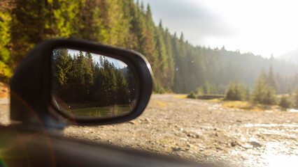 Car parked on road with forest in the background, sunlight shining on the mirror reflecting the green forest, natural setting for outdoor activities