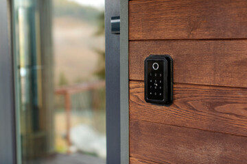 Keyless entry system mounted on wooden wall beside glass door, device is easily accessible