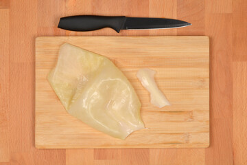 A trimmed leaf of fermented pickled cabbage lies on a wooden board next to a black knife and the...