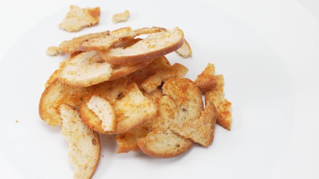 A small pile of baked bread chips rotates gently on a white surface. The video focuses on crisp edges, seasoning, and snack texture using smooth rotation.