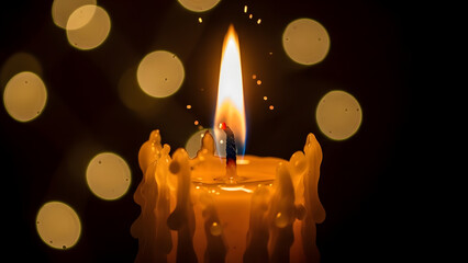 Warm glowing candle flame burning brightly with melted wax drips and soft golden bokeh lights creating a tranquil and peaceful atmosphere in darkness
