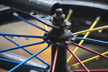 Close-up of a bicycle wheel hub with colorful spokes and water droplets after rain.