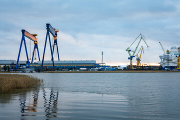 Obraz premium Photo of a large ship being constructed at a shipyard near the sea, captured from a distant vantage point. Shows cranes, scaffolding, massive vessel structure, and industrial maritime environment.