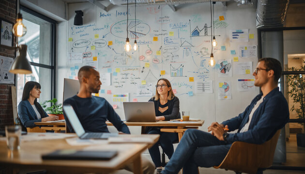 A creative team from a startup gathers in a modern, open-plan office for a brainstorming session. Whiteboards are covered in sketches and notes, laptops are open, and expressions are relaxed yet focus - Powered by Adobe