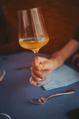 A hand is holding a glass filled with a yellow drink. The setting includes a blue tablecloth and a fork nearby, suggesting a dining atmosphere where people gather