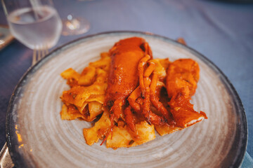 A seafood dish is placed on a white plate. The meal features squid and pasta. The setting shows a table prepared for dinner with utensils and glasses nearby