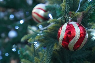 Red and gold striped Christmas ornament hangs gracefully on a lush green tree branch, surrounded by twinkling lights. The image captures the essence of holiday decoration