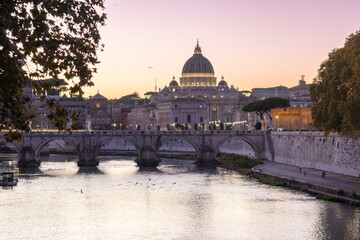 View of St. Peter's Basilica in Vatican City and the Sant'Angelo Bridge from the Umberto I Bridge at sunset in Rome, Italy.