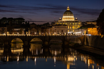 Fototapeta premium View of St. Peter's Basilica in Vatican City and the Sant'Angelo Bridge and the Tiber River, from the Umberto I Bridge, at dusk in Rome, Italy.