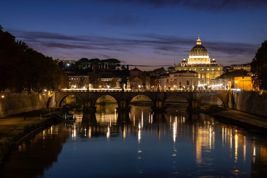 View of St. Peter's Basilica in Vatican City and the Sant'Angelo Bridge and the Tiber River, from the Umberto I Bridge, at dusk in Rome, Italy.