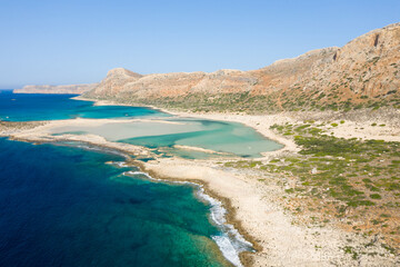 A vibrant turquoise lagoon meets rocky coastline at Balos Beach in Crete, Greece, framed by sunlit cliffs and clear blue sky. The landscape feels pristine, expansive, and inviting.