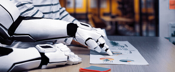 A futuristic robot collaborates with a human in a modern office, analyzing documents featuring colorful graphs and charts, symbolizing advanced technology and teamwork.Noogenesis